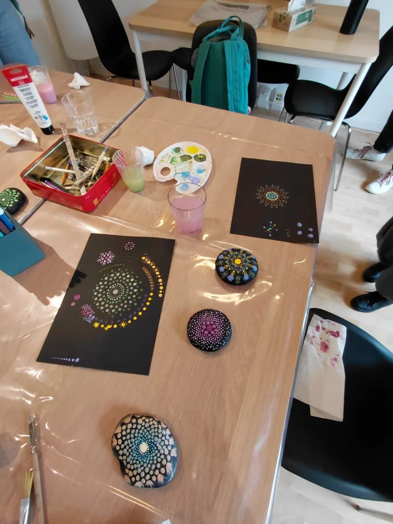 Mandalas en points sur papier noir et galets peints, posés sur la table de l'atelier.
