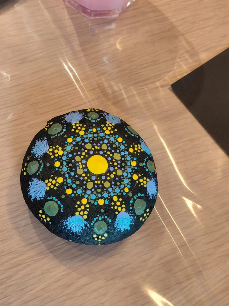 Un galet décoré d'un mandala en points jaunes, bleus et verts.