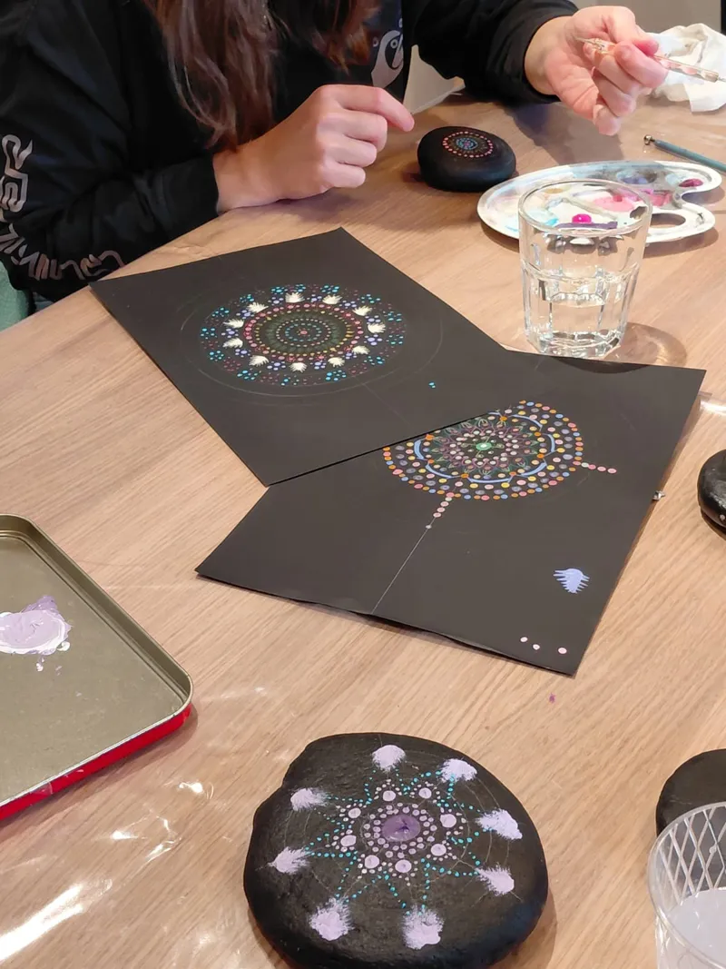 Deux mandalas en points sur papier noir et un galet peint, en cours de réalisation.