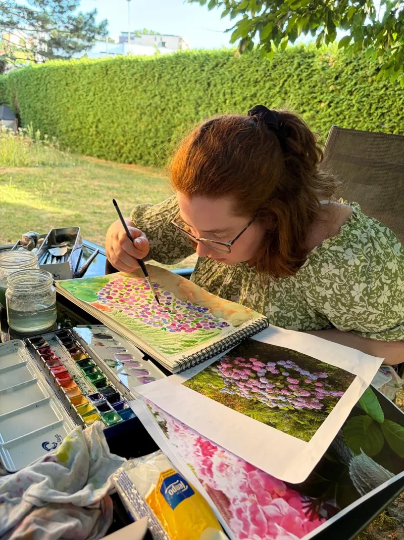 Une participante concentrée sur son aquarelle de fleurs pendant un cours au jardin.