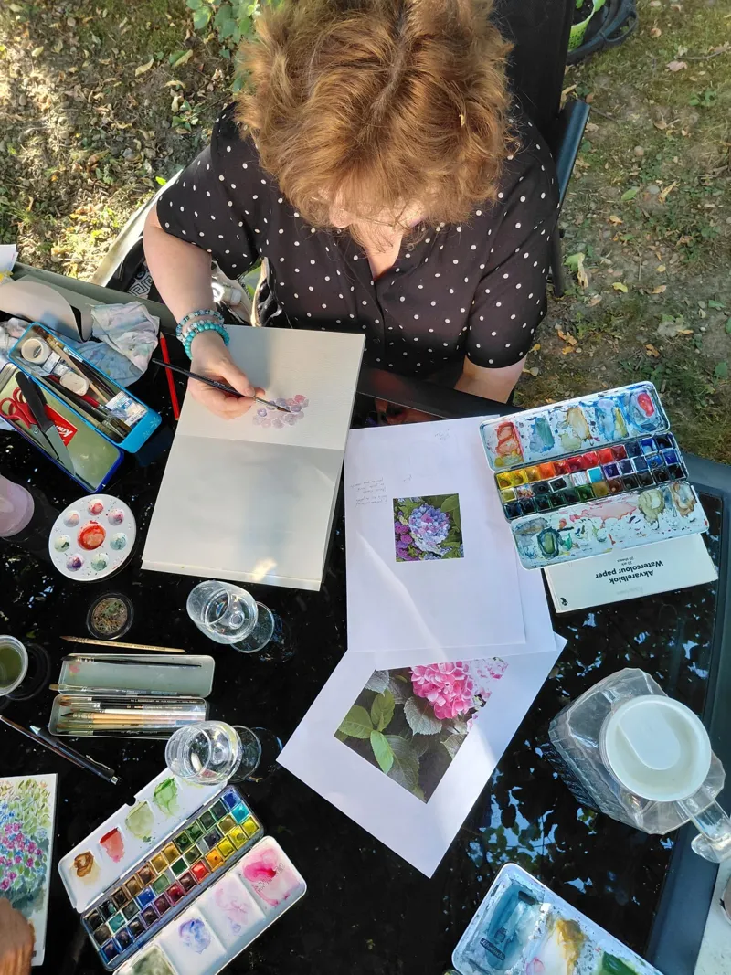 Cours pour adultes en plein air : participants peignant autour d'une table.