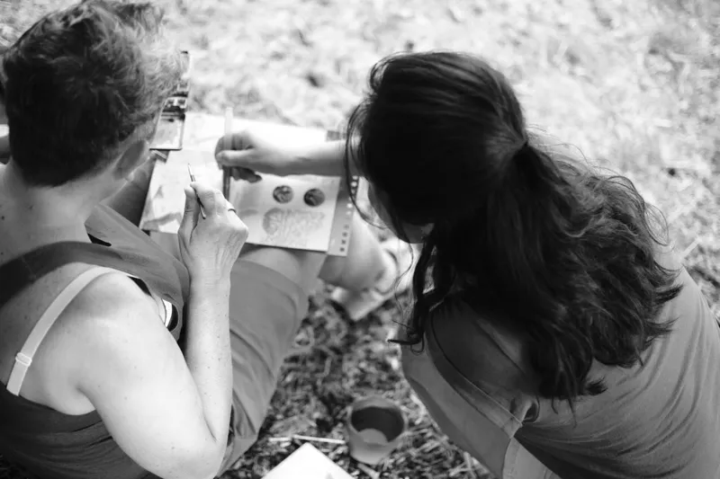 Roxana se penche vers une participante et lui donne des conseils sur son aquarelle.
