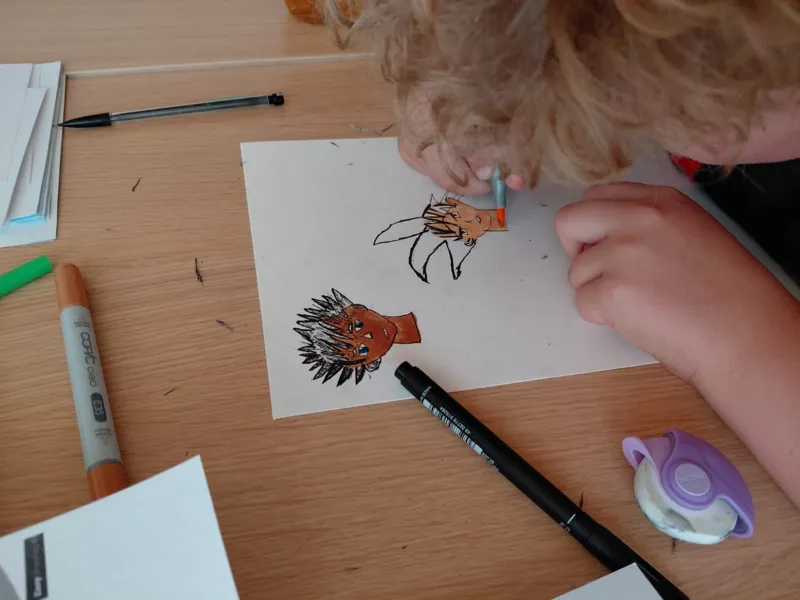 Atelier manga : des enfants dessinent et colorient leurs personnages aux feutres.
