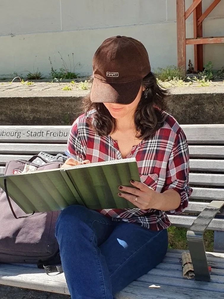 Roxana Rodriguez dessine dans son carnet, assise sur un banc à Fribourg.